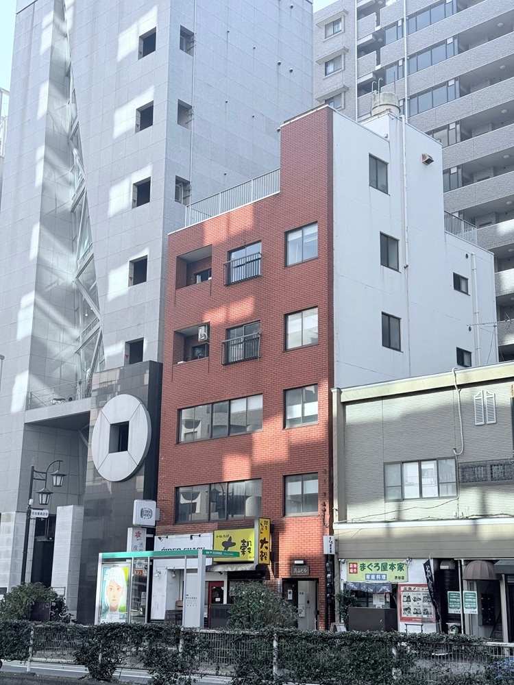 外観（明治通り沿いの雑居感のあるビル。窓超し・屋上に人を立たせて実景撮影も可能）